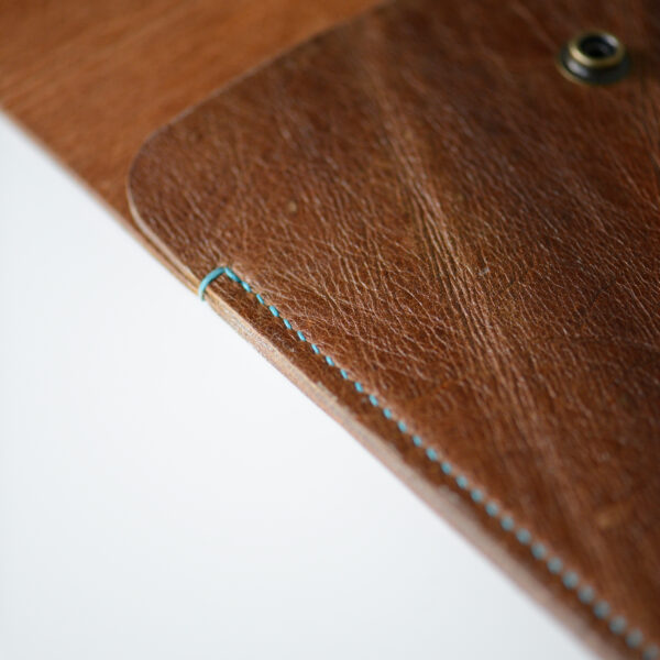 Side view of tan leather laptop case, hand stitched with blue linen thread