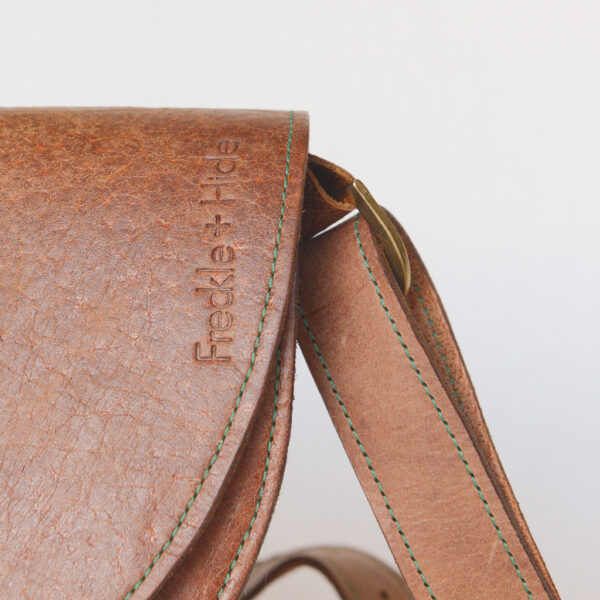 Close up of tan leather shoulder bag showing silver hardware, green stitching and the F+H logo embossed vertically