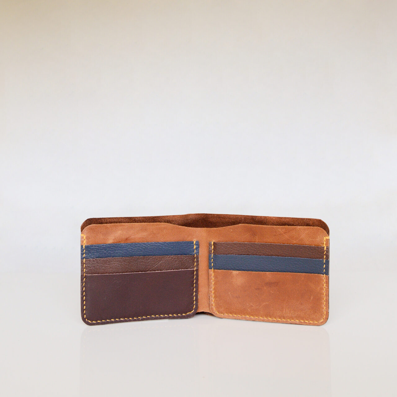 Inside view of leather bifold wallet. Tan, brown and dark blue leather with yellow stitching.