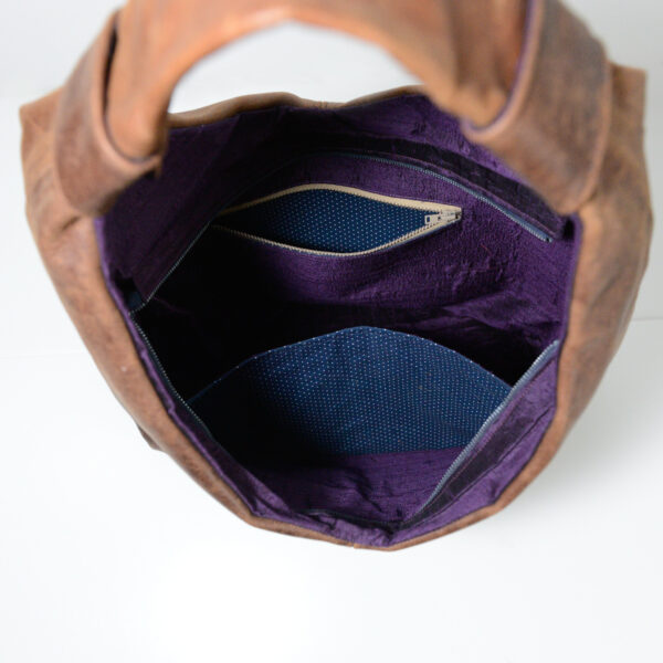 Inside view of brown reclaimed leather bag showing purple shot silk lining and dark blue polkadot pocket lining fabric